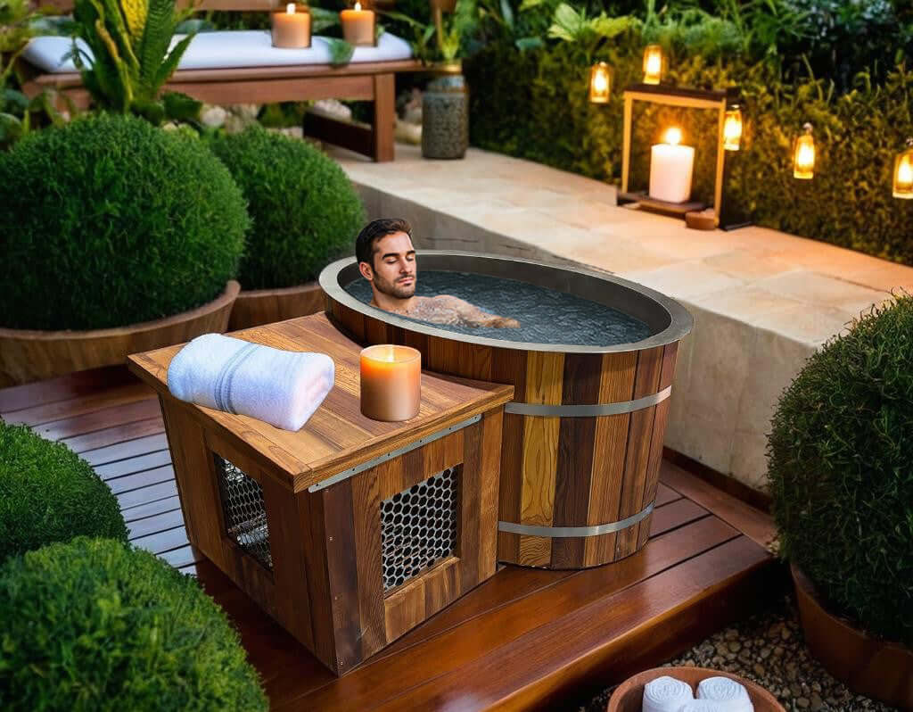 Man relaxing in Rustic Oval ice bath with candle and towels in a serene garden setting.